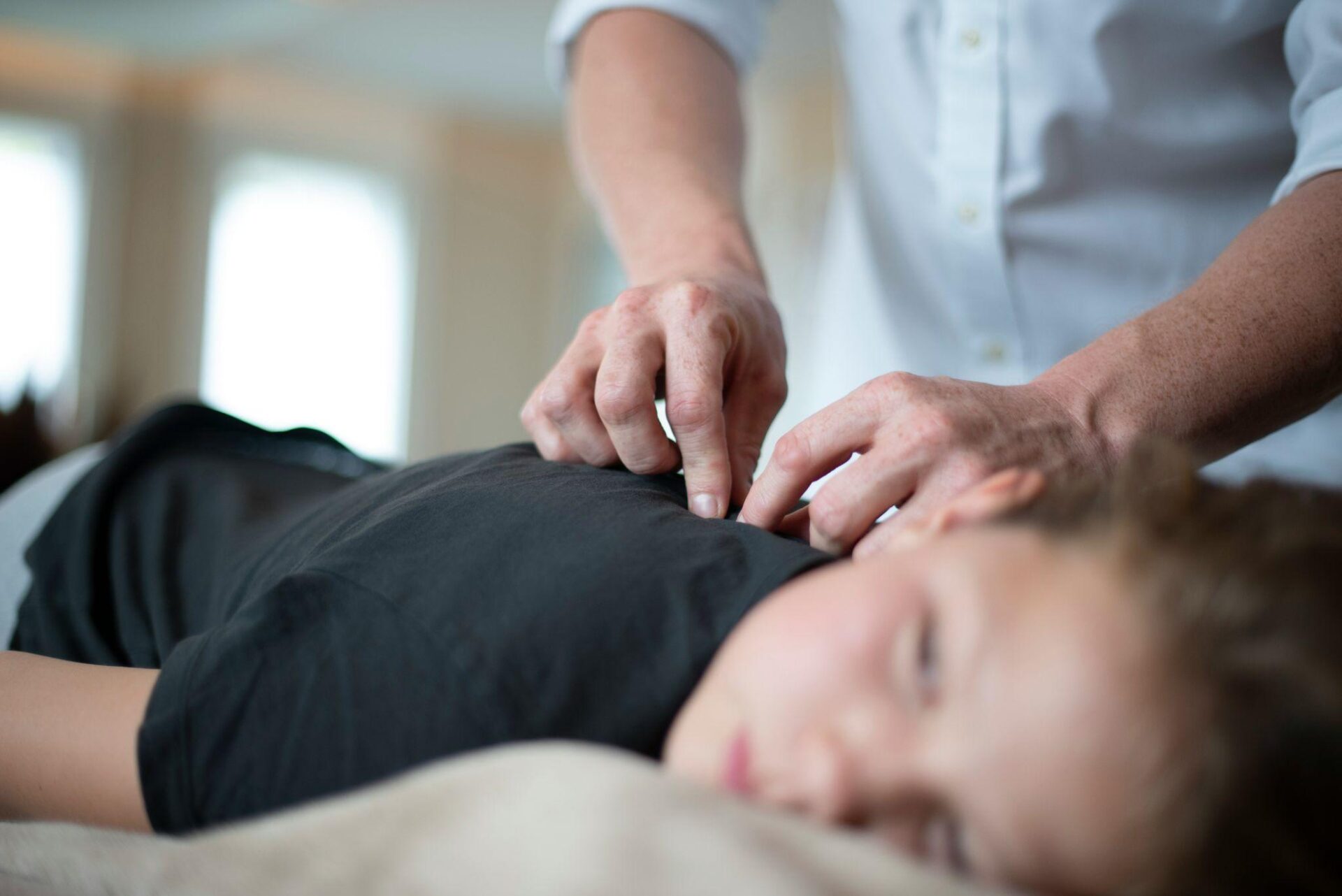 Clinical massage therapist applying targeted pressure to a patient’s upper back during a treatment session for chronic pain relief.